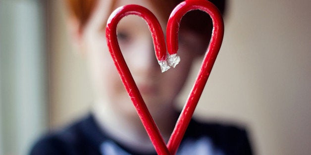 Young boy holding two red candy canes together to form a heart