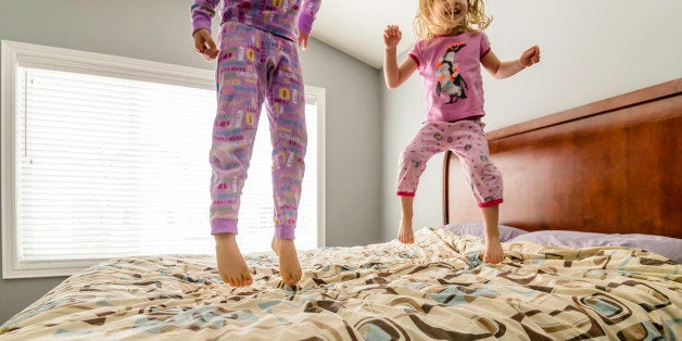 Two young girls jumping on a bed in pajamas