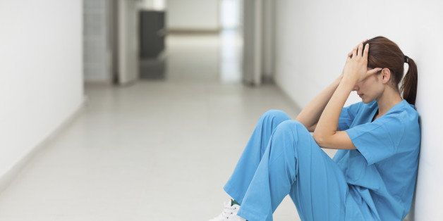 Nurse sitting in a corridor while holding her head in a hospital