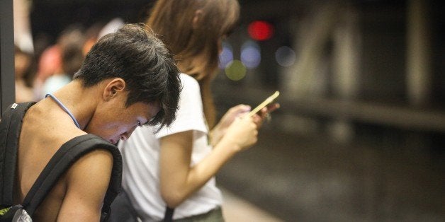 Japanese young people using smartphone on the platform of a railway station while they are waiting for the train. (rarely seen shirtless style in Jspan)