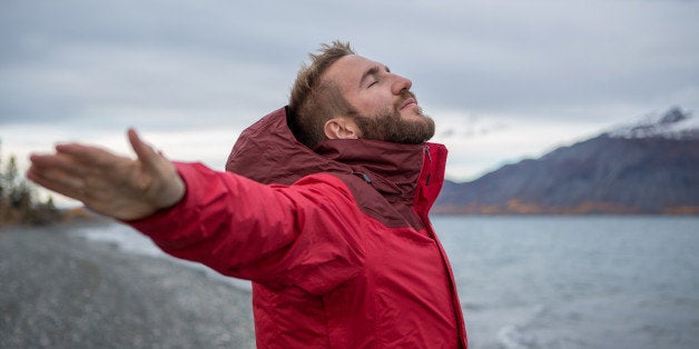 Young cheerful man by the lake enjoying nature. Arms outstretched for positive emotion. 