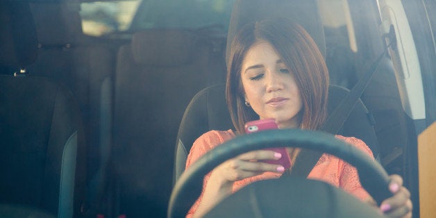 Portrait of a young woman texting on her smartphone while driving a car