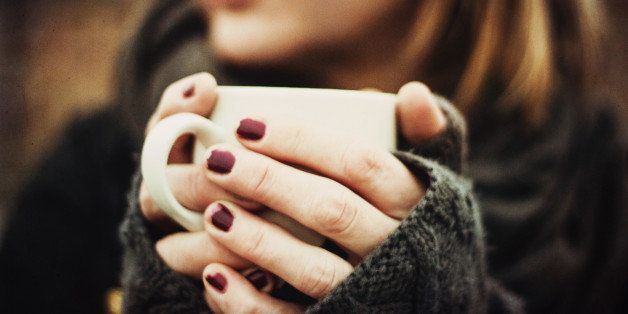 A woman holding a hot drink in gloved hands.