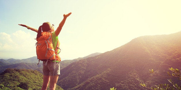 cheering woman hiker open arms at mountain peak cliff