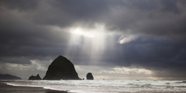 'Landscape of Cannon Beach, Oregon in the winter during a stormfront. A sliver of light shines down over Haystack Rock. Focus on the water.'