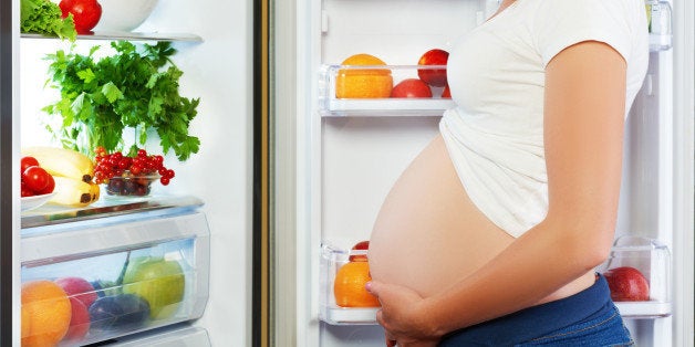 nutrition and diet during pregnancy. Pregnant woman standing near refrigerator with fruits and vegetables