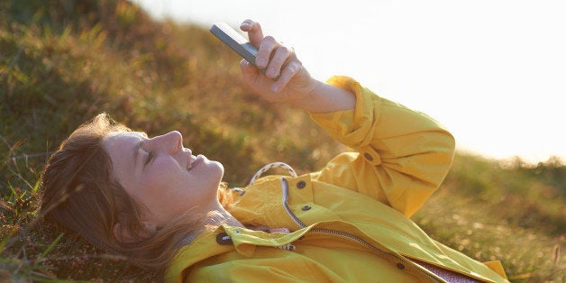 A woman lays down in the grass and uses her phone.