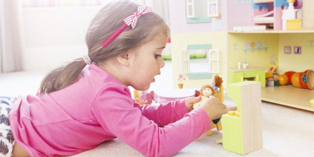 Young girl plays with dolls in dolls house.