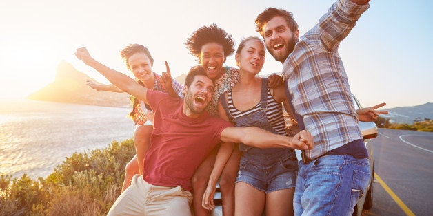 Group Of Friends Standing By Car On Coastal Road At Sunset