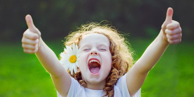 Laughing girl with daisy in her hairs, showing thumbs up.