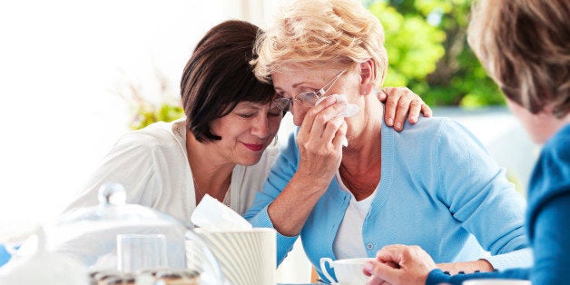 Senior women sitting at the table at home and comforting ther unhappy friend.