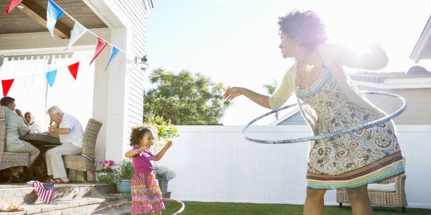 Cheerful mother and daughter twirling hula hoops on lawn