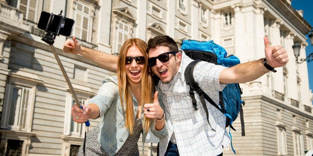 young beautiful friends tourist couple visiting Spain in holidays exchange students and taking selfie stick picture together in town happy on sunny day in travel and vacation concept