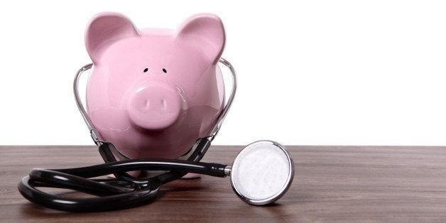 Traditional pink piggy bank with stethoscope standing on a wood table. Space for copy.