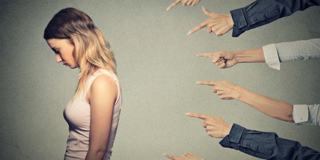 Concept of accusation guilty person girl. Side profile sad upset woman looking down many fingers pointing at her back isolated on grey office wall background. Human face expression emotion feeling