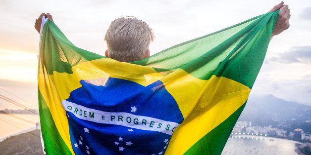 A young man with a colorful brazilian flag around his back at sunset on the top of Sugarloaf mountain in Rio.