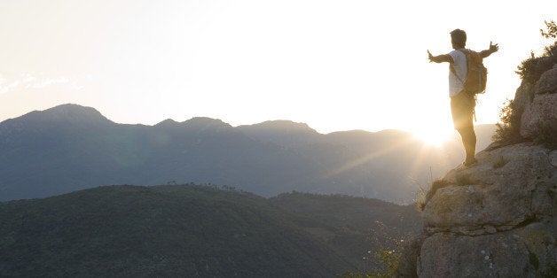 Hiker standing on bluff, arms outstretched