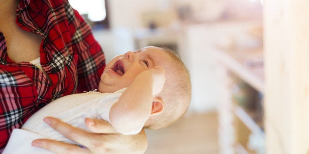 Crying little baby in the arms of her mother in a living room.