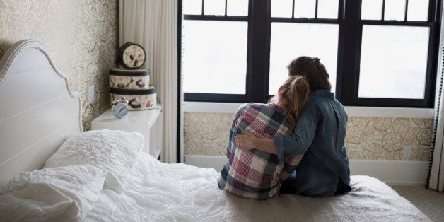 Mother hugging teenage daughter in bedroom