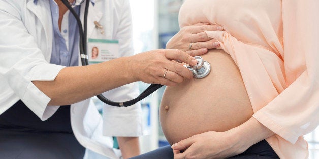 Doctor using stethoscope on pregnant patients stomach