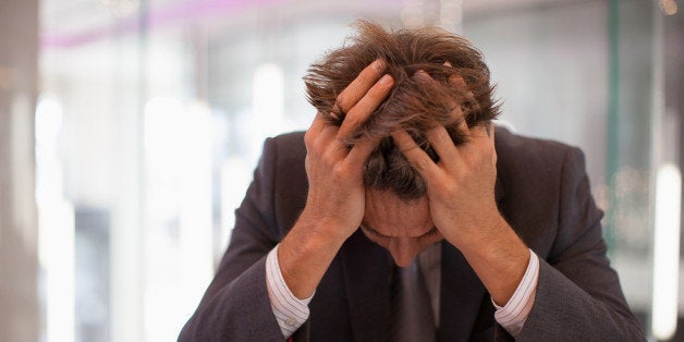 Frustrated businessman sitting at desk with head in hands