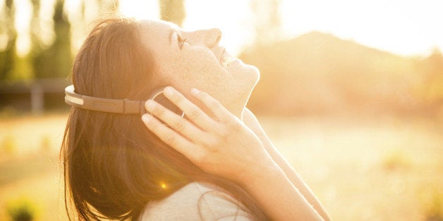 Young happy caucasian woman listening music in the nature with her modern ear phone, during the sunset.