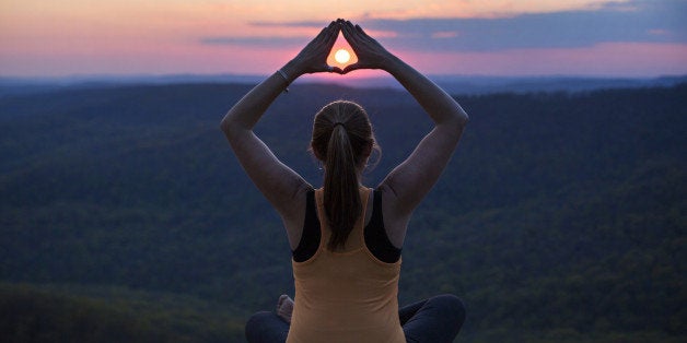 Woman meditates on a mountain top at sunset at White Rock Mountain in Arkansas.