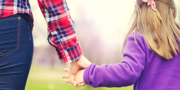 Mother is walking with her daughter in the park and holding hands. A closeup, rear view, AdobeRGB profile.