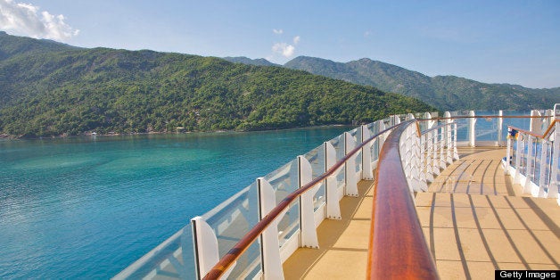 Teak handrails and shadows of cruise ship near clear blue Caribbean Sea waters and lush hills on north coast of Haiti