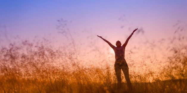 silhouette of a woman lifting her hands in worship, in a meadow at sunset.