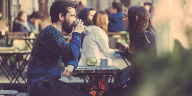 Hipster couple drinking coffee in Stockholm old town. They're sitting face to face. The man is wearing a blue sweater and the woman a striped shirt with black leather jacket.