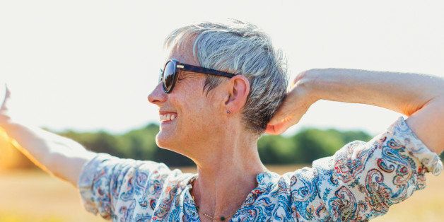 Enthusiastic senior woman with arms outstretched in sunny field