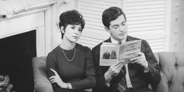 Couple sitting in lounge room, man reading book, (B&W)