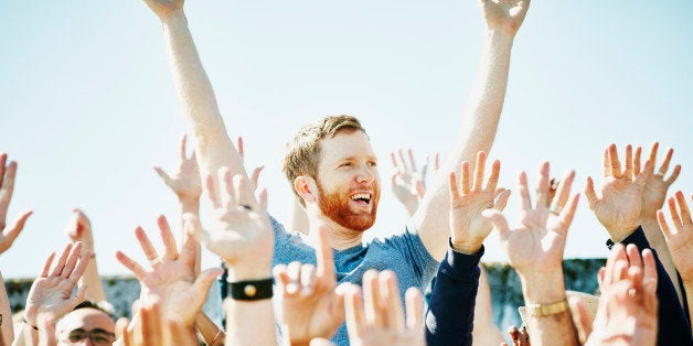 Smiling man standing with arms raised overhead in cheering crowd in stadium at sporting event