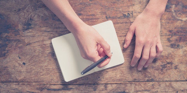 Close up on the hands of a young woman as she is writing in a small notepad at a wooden table