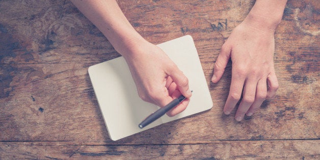 Close up on the hands of a young woman as she is writing in a small notepad at a wooden table