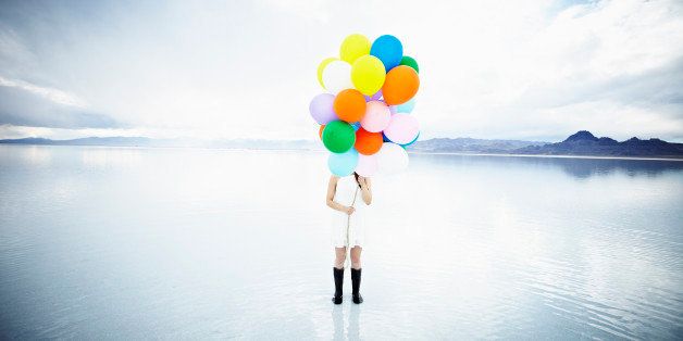 Woman standing in water on salt flats holding bunch of balloons hiding face