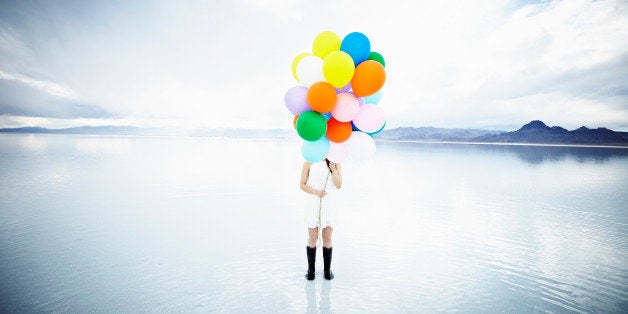 Woman standing in water on salt flats holding bunch of balloons hiding face