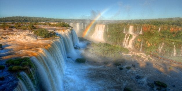 Iguazu falls and rainbow against blue sky.