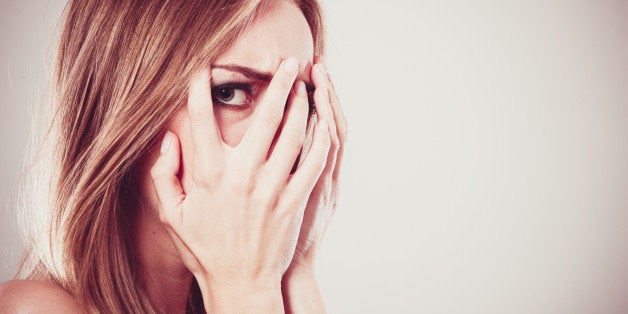 Afraid frightened woman peeking through her fingers on grey. Shy teen girl covering face with hands.