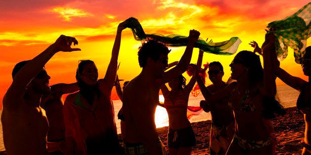 Tropical beach party. Spring break backlit image of a group of more than ten teenagers or young women and men dancing at sunset on a tropical beach. People wearing swimsuits and dancing on the sand of a tropical Caribbean island beach in Morrocoy, Venezuela. Image taken at sunset during short vacations with people in the foreground and the sea and sun in the background, Predominant color: yellow. Backlit DSLR outdor photo taken with a Canon 5D Mk III.