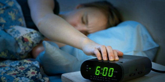 Young woman pressing snooze button on early morning digital alarm clock radio