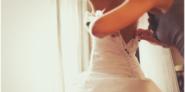 A shot of a bride getting into her wedding dress taken from a lower angle as the back of the dress is being done up from the help of her mother.