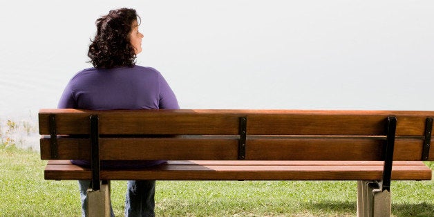 rear view of overweight woman sitting on park bench near lake