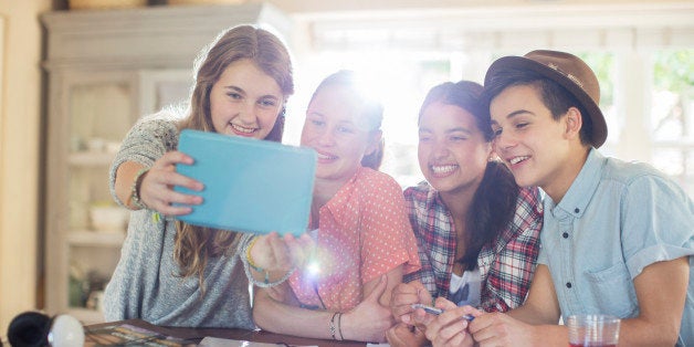 Group of smiling teenagers taking selfie in dining room