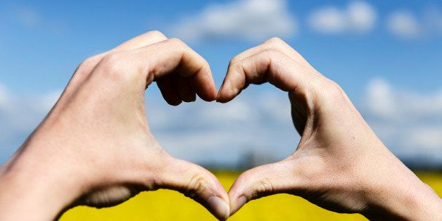 Beautiful Love shape hands - heart on yellow field and blue sky