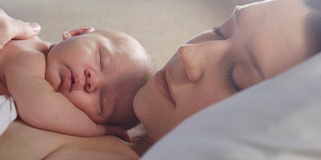 Mother sleeping with newborn baby on bed