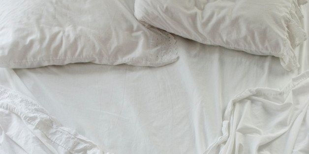 High angle view of unmade bed with rumpled white sheets and two pillows in soft early morning light