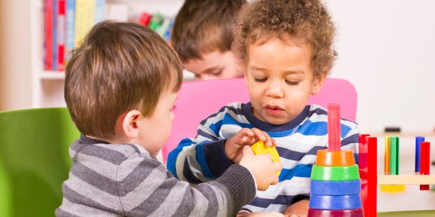 A stock photo of a caucasian and african american child sharing in the play room.