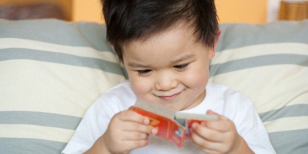 Cute toddler boy with amusing smirk on face reading small board book.